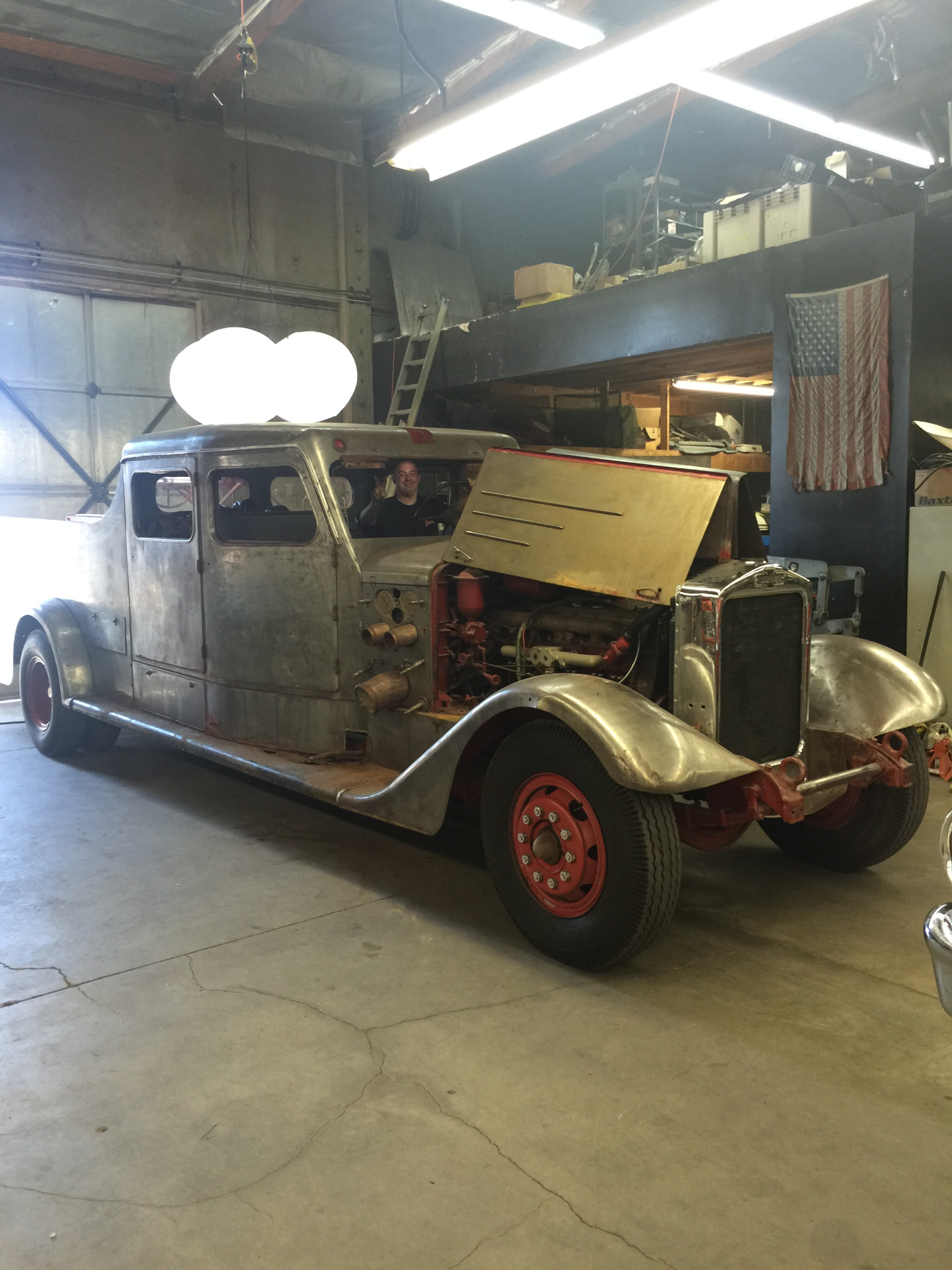 In the shop mid-build: bare metal body, hood open over the inline six