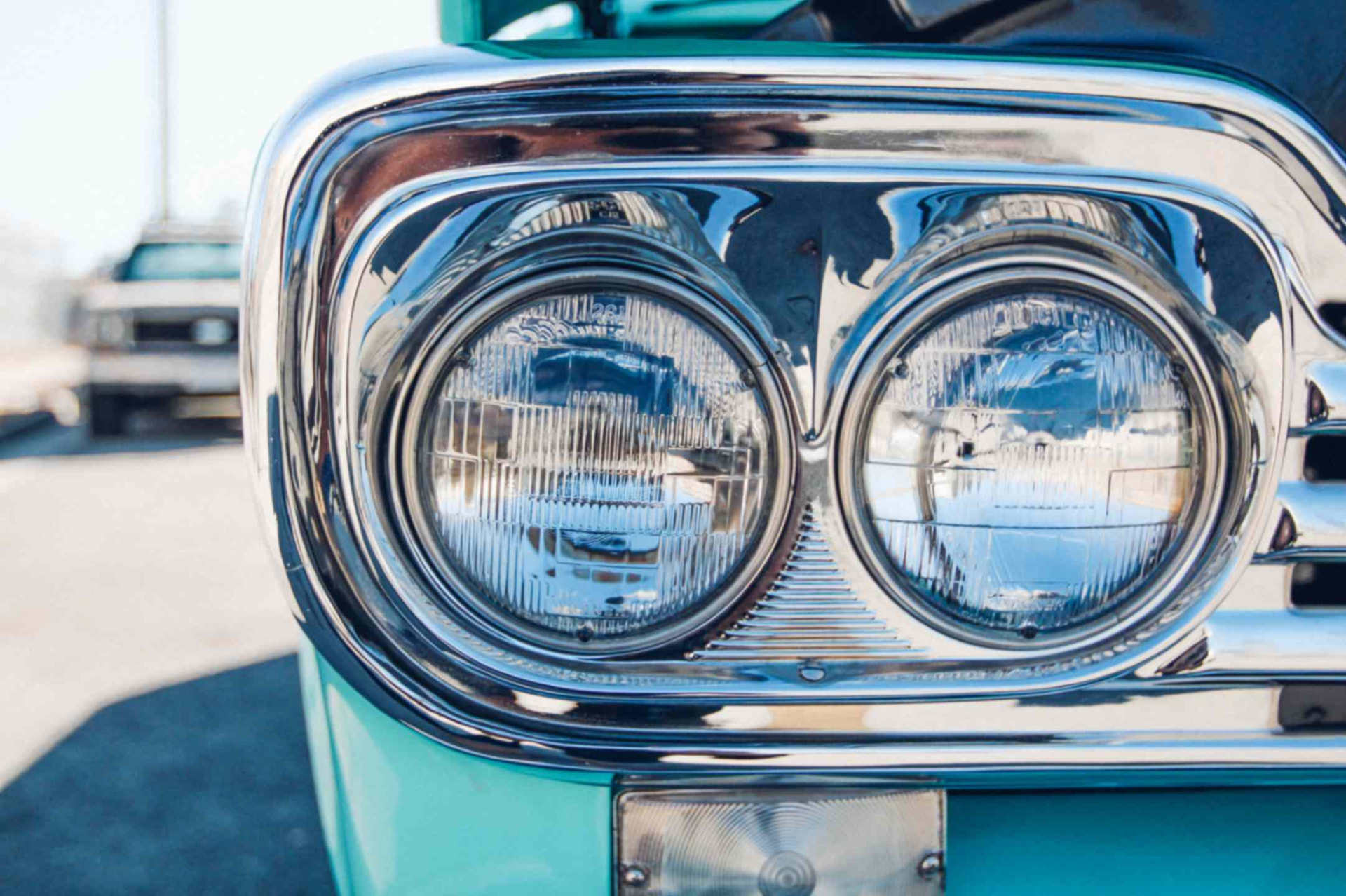 Dual headlamp and chrome bezel close-up on the turquoise fender